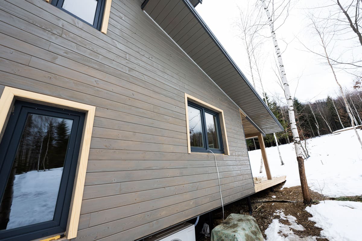 Exterior wall of a modern house in Lowell, MA, with gray vinyl siding that looks like wood, black framed windows, and light trim around the frames.